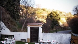 Terrassa exterior amb taules i caires blancs, una petita zona de jardí i una paret blanca amb una porta.