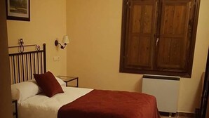 Una habitació amb dos llits, un armari de fusta, una taula petita i una làmpada penjada a la paret.
