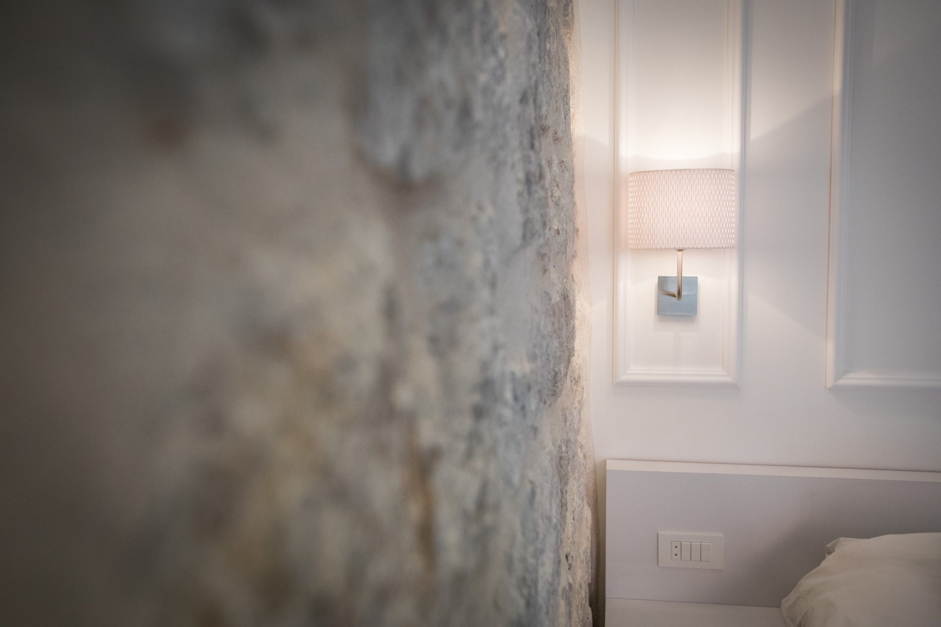 Une chambre avec un mur à texture, une lampe de chevet et un lit blanc.