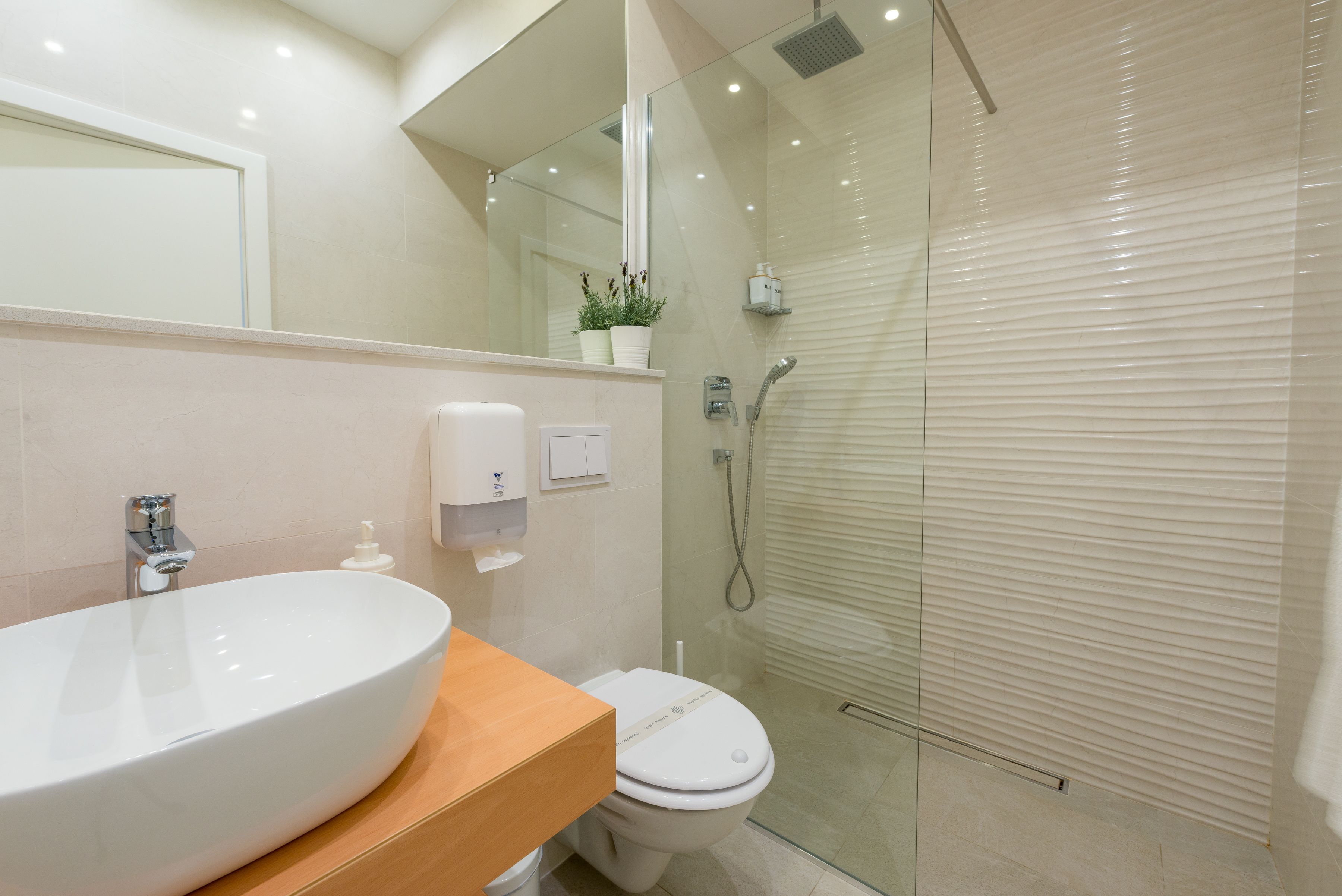 A modern bathroom with a large oval sink, a toilet, and a glass-enclosed shower.