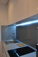 Cozinha moderna com pia de aço inoxidável, fogão por indução preto e tábua de corte de madeira.