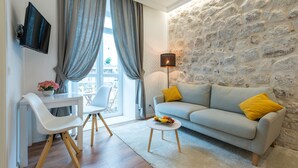 A modern living room with a stone wall, a grey sofa with yellow cushions, a white table, and a white chair. - Scalini Palace (Dubrovnik)