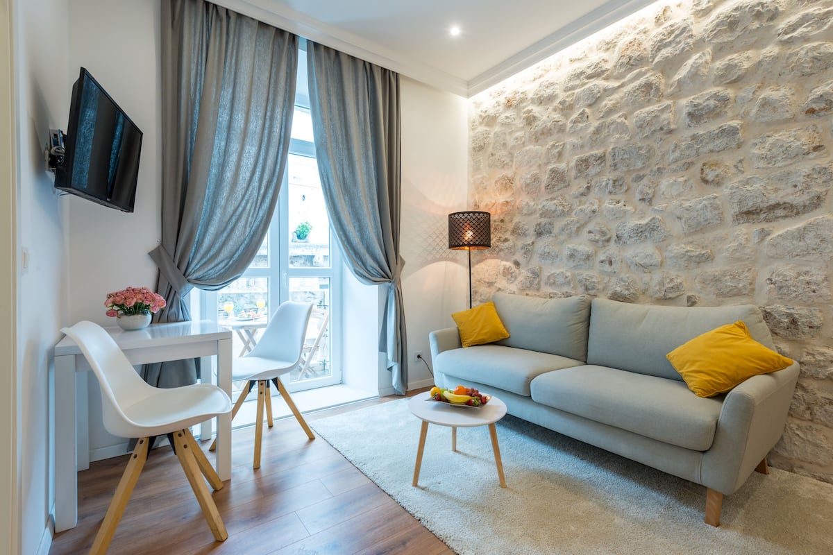 A modern living room with a stone wall, a grey sofa with yellow cushions, a white table, and a white chair.