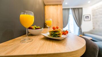 Un desayuno con una mesa de madera, dos vasos de jugo de naranja, un plato con un sándwich y tomates, y un bol de ensalada.