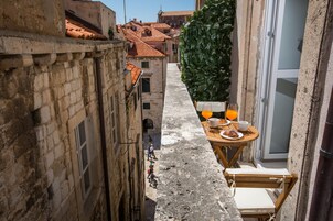 Uma passagem estreita com uma mesa posta para o café da manhã, uma parede verde e edifícios com telhados de telha vermelha.