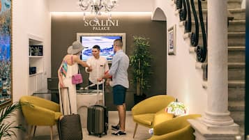 Un área de recepción con un cartel de 'Scalini Palace', una araña y escaleras, además de sillas amarillas.