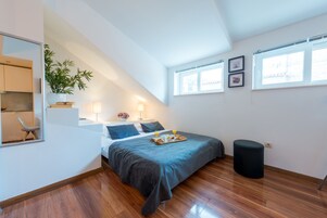 Un dormitorio moderno con cama, mesita de noche, lámpara y un pequeño taburete.