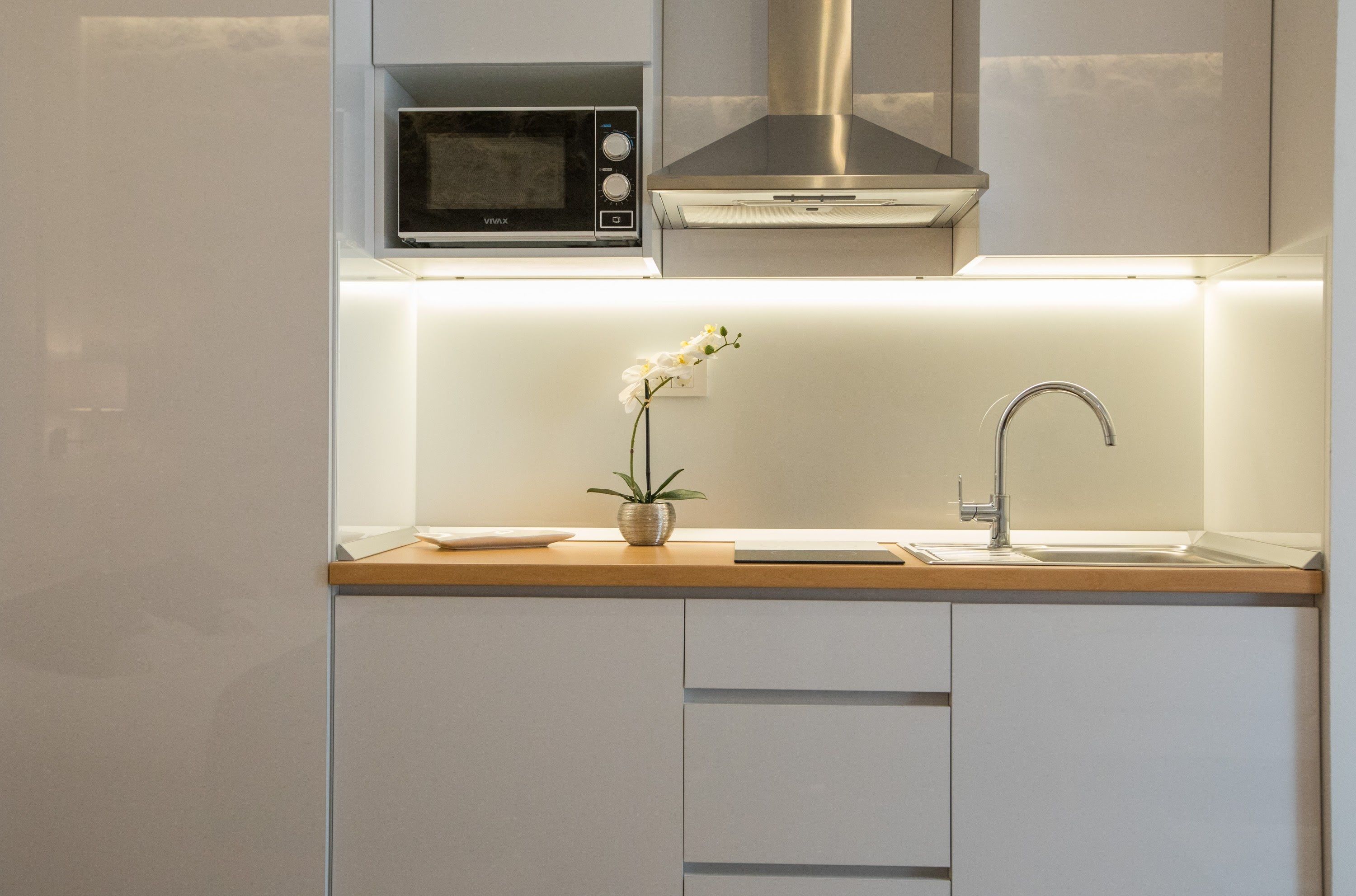 Une cuisine moderne dotée d’un four à micro-ondes encastré, d’une hotte en acier inoxydable et d’un design minimaliste.