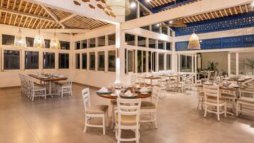Un vaste espace dédié à la salle à manger, avec de nombreuses tables et chaises, de grandes fenêtres et des luminaires suspendus.