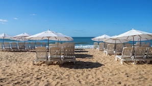Een strand met rijen witte ligbedden en parasols, gericht op de oceaan.