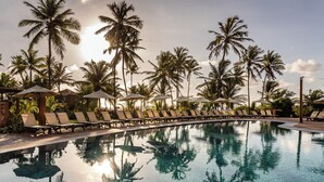 Un espace aménagé au bord de la piscine, avec des chaises longues et des parasols, entouré de palmiers.
