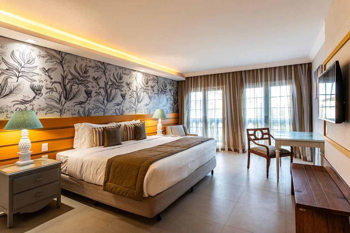 Habitación de hotel con una cama grande, un escritorio, una silla, un televisor y una ventana con cortinas.