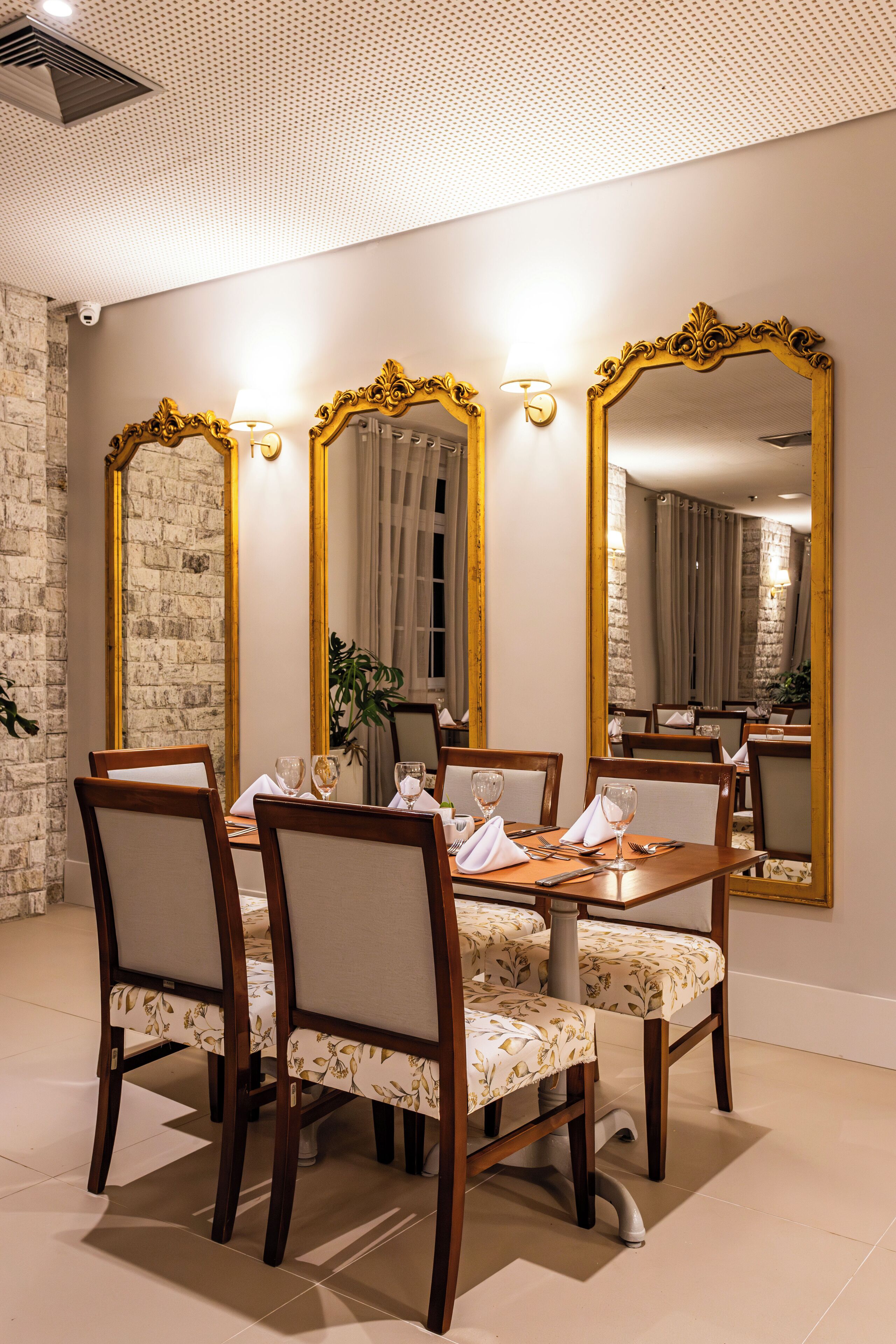 A dining area with a round table, six chairs, and three large mirrors with gold frames.