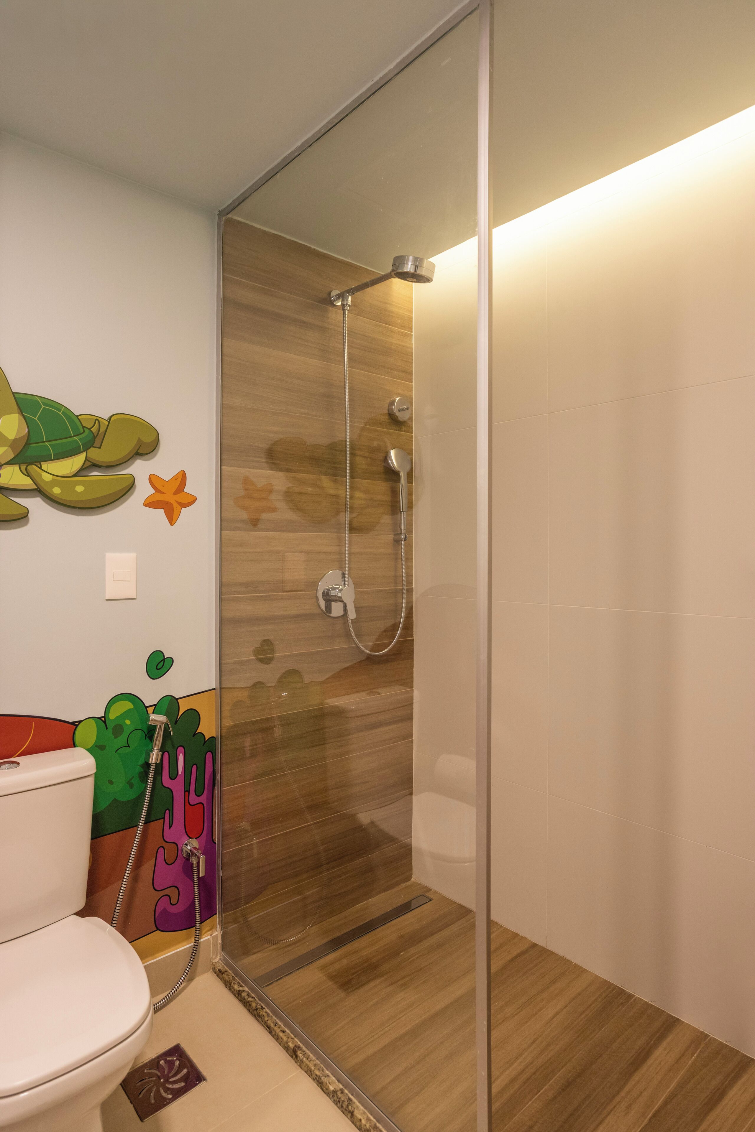 A bathroom with a glass-enclosed shower, a toilet, and a wall with a mural.