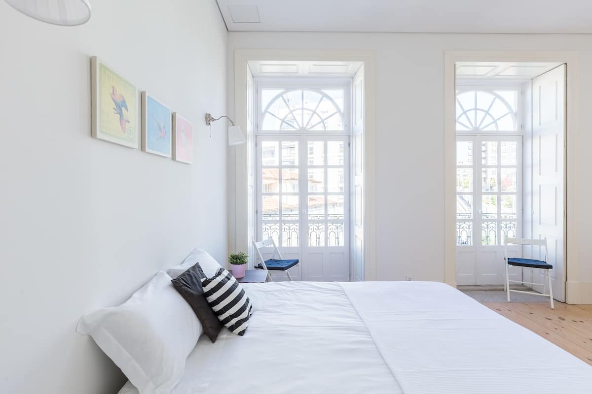 A bedroom with a large bed, two chairs, a window, and artwork on the wall.