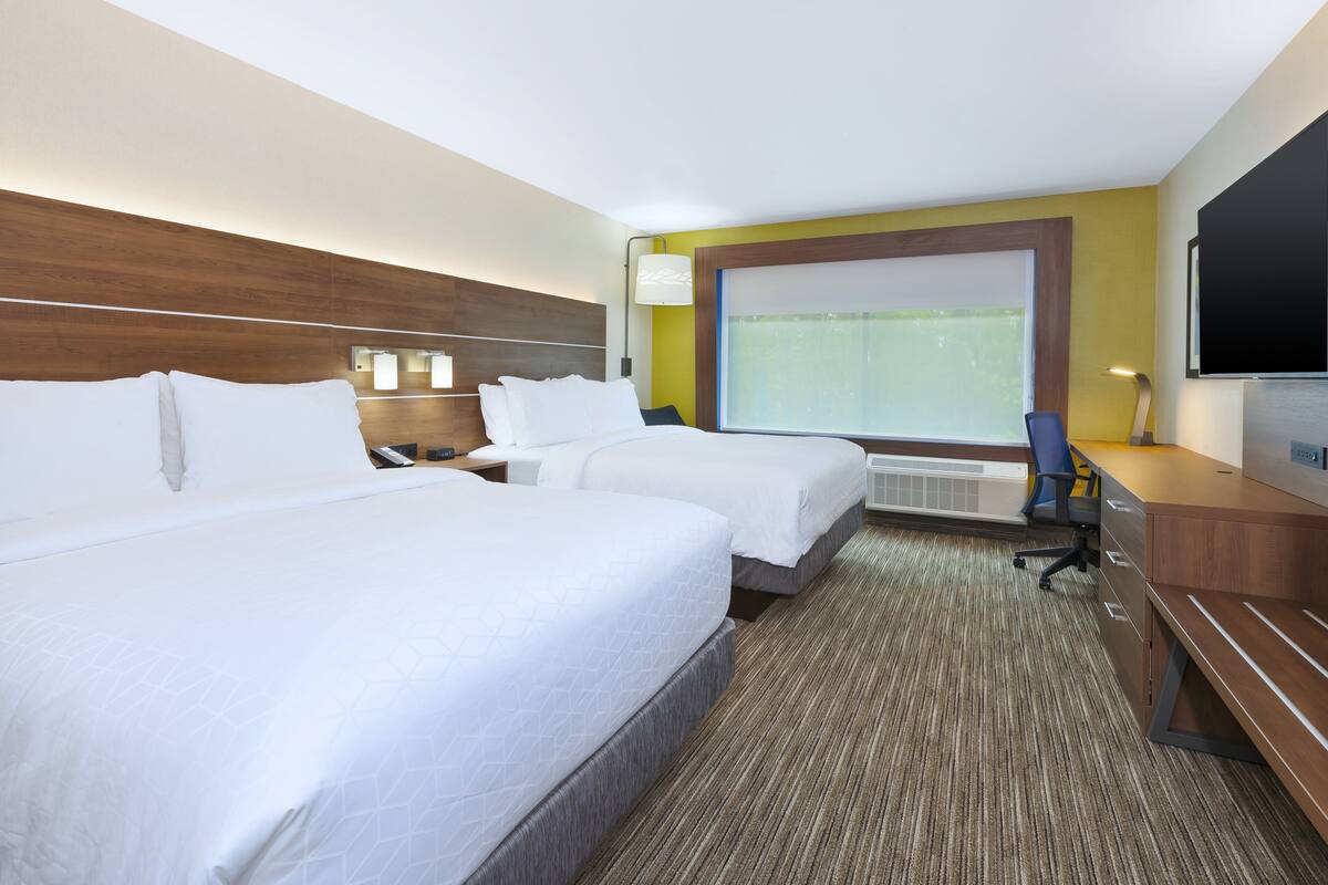 A hotel room with two beds, a desk, a chair, a TV, and a large window.