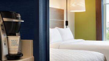 A hotel room with a coffee maker, a cup, and a bed with white bedding.