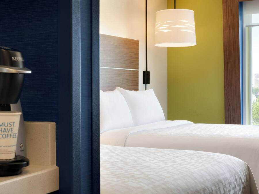 A hotel room with a coffee maker, a cup, and a bed with white bedding.