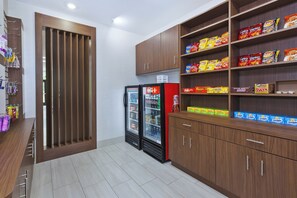 A snack and beverage section with shelves stocked with various brands, a refrigerator, and a wooden cabinet. - Holiday Inn Express & Suites Painesville - Concord by IHG (Painesville)