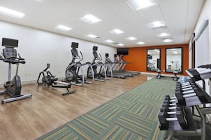 Un gimnasio con cintas de correr, bicicletas estáticas y una máquina de remo.