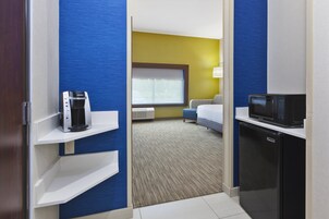 Habitación de hotel con kitchenette, cama, ventana con persianas y vista al exterior.