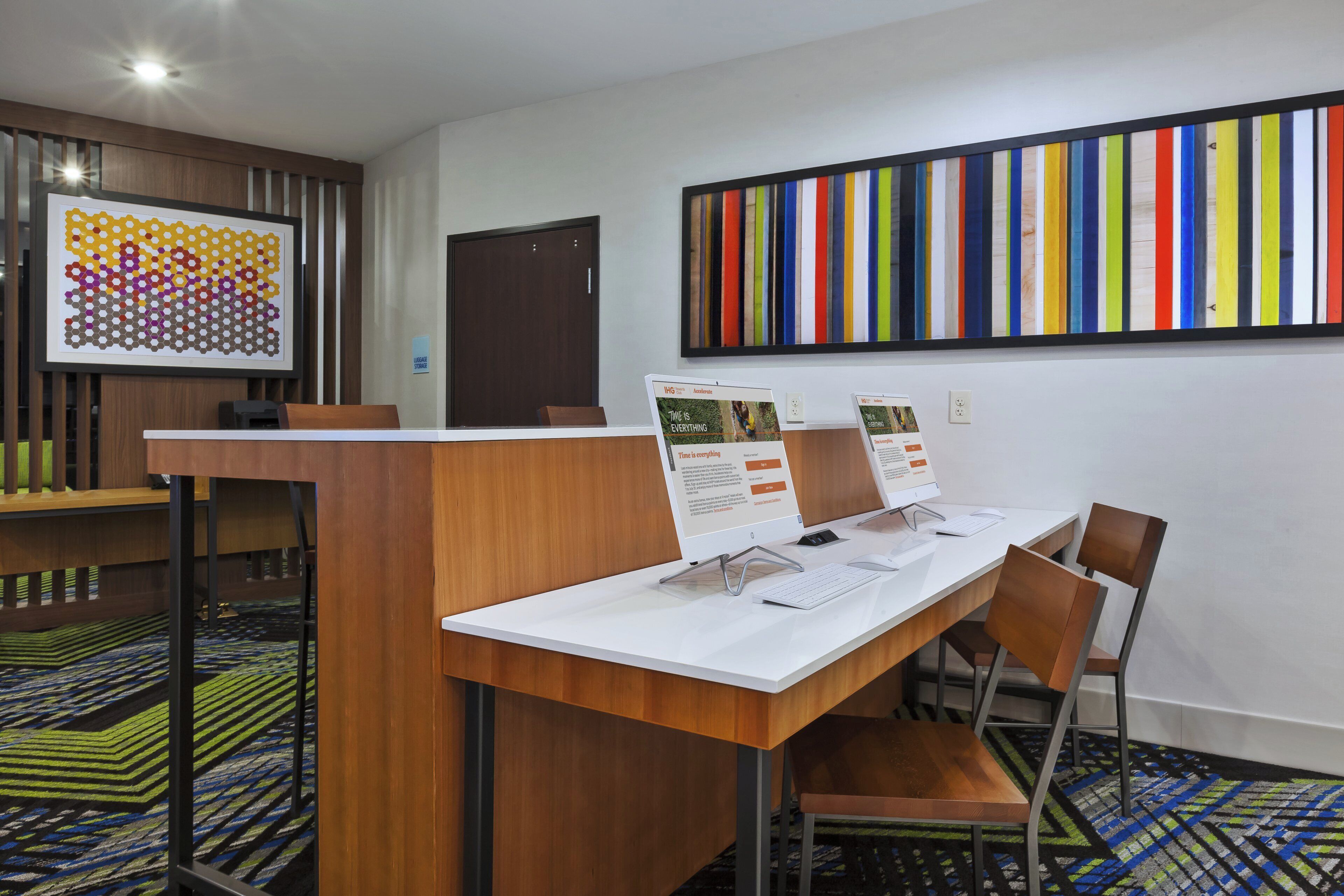 Een hotel receptie met een receptiebalie, stoelen, een groot kleurrijk kunstwerk aan de muur en een kamerbreed tapijt met dessin.