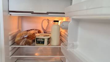 An open refrigerator with shelves containing a loaf of bread, a carton of milk, and a container of Olivani yogurt.