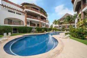 Un complexe hôtelier doté d’une grande piscine incurvée, entourée de chaises longues et d’un jardin bien entretenu.