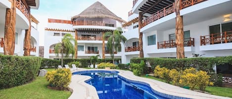A resort with a central swimming pool, multiple balconies, and lush greenery.