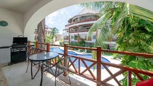 A balcony with a grill, table, and chairs, overlooking a pool and a building with balconies. - Xaman 201   by NAS (Playa del Carmen)