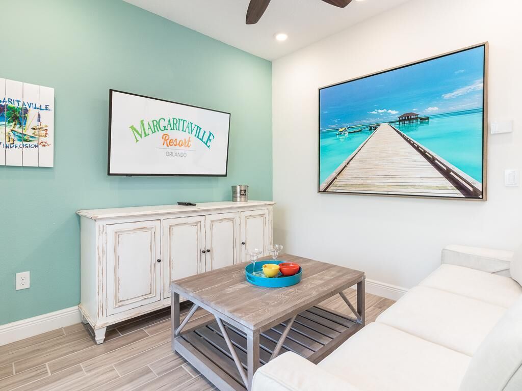 A room with a teal wall, a white cabinet, a wooden coffee table with a tray, and a large framed picture of a beach scene.