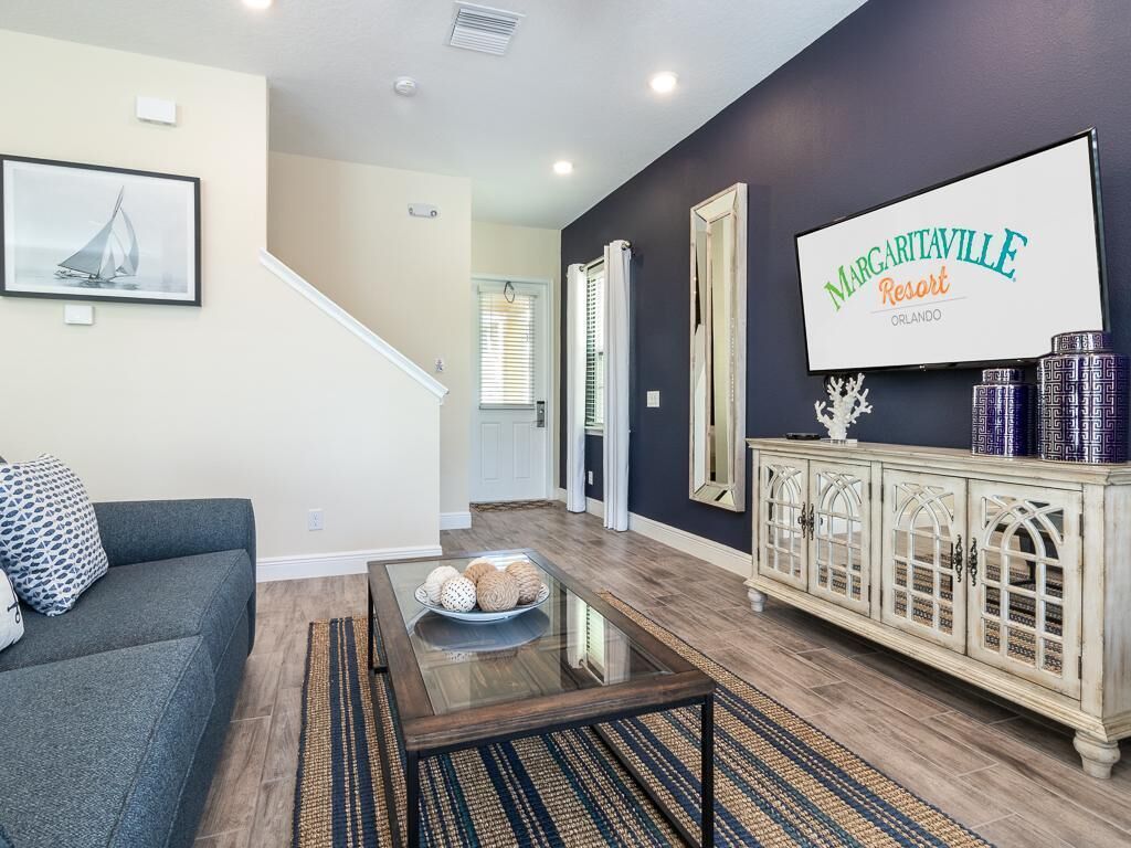 Un salón con una pared oscura, un sofá, una mesa de centro con objetos decorativos, un mueble con jarrones estampados y un letrero de MARGARITAVILLE Resort.