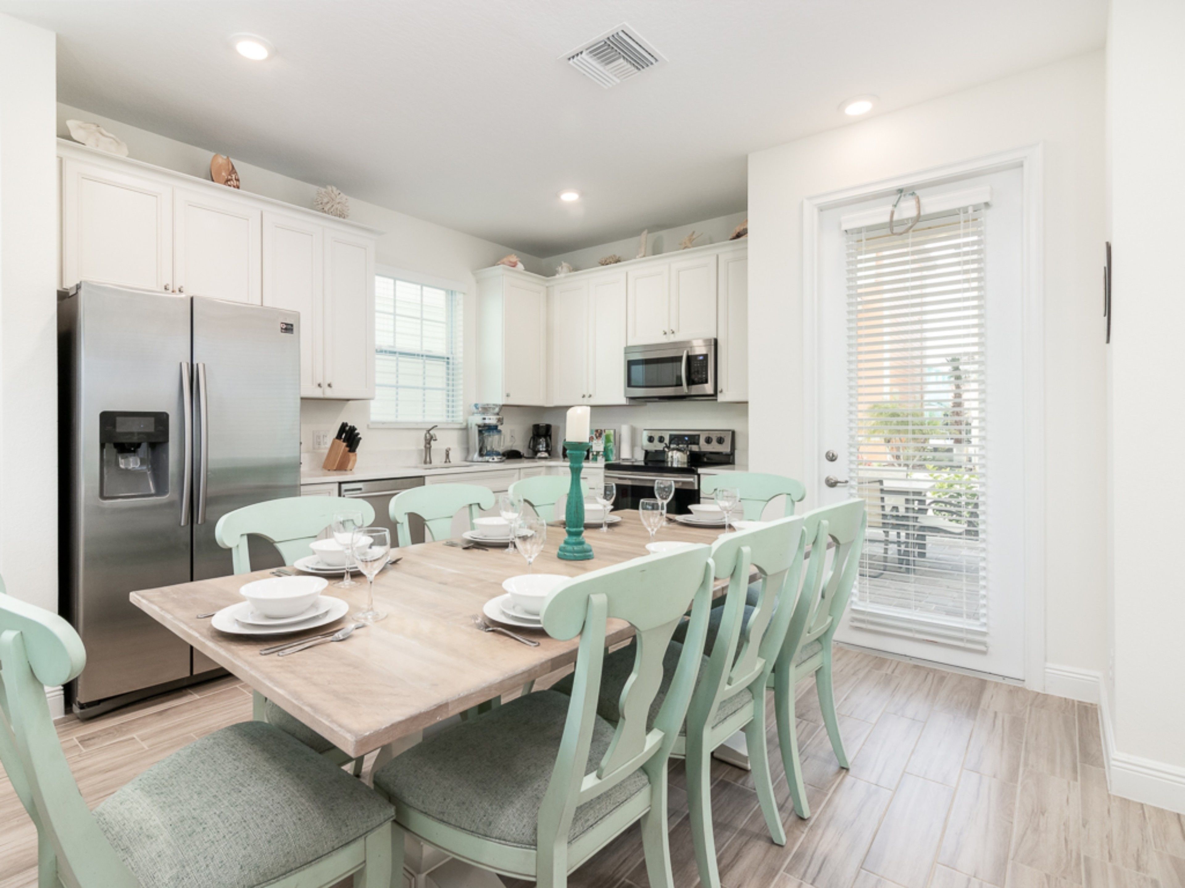 A modern kitchen with white cabinets, stainless steel appliances, and a dining area with light green chairs and a wooden table.