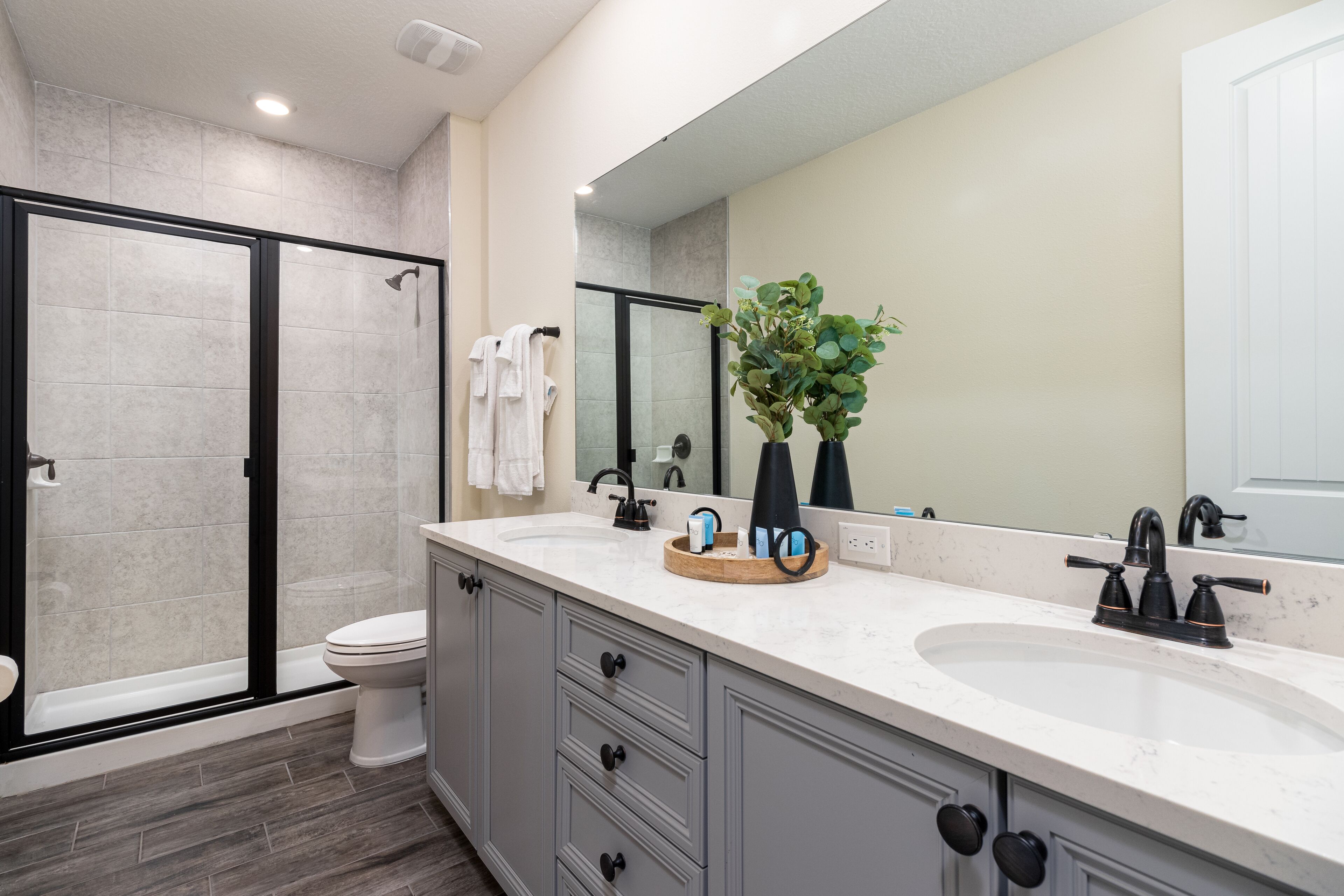 Une salle de bain moderne avec une douche à parois de verre, des toilettes blanches et un meuble-lavabo doté d’un grand miroir.