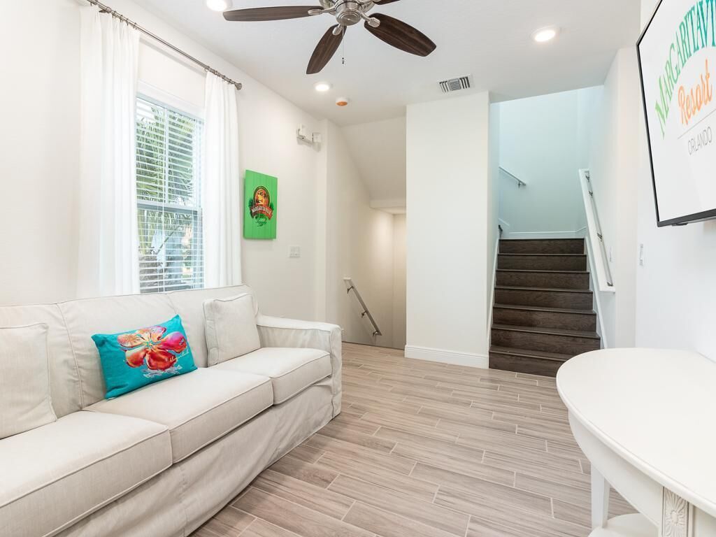 Una sala de estar con un sofá color beige, un cojín verde azulado, una bañera blanca y una escalera que sube a otro nivel.