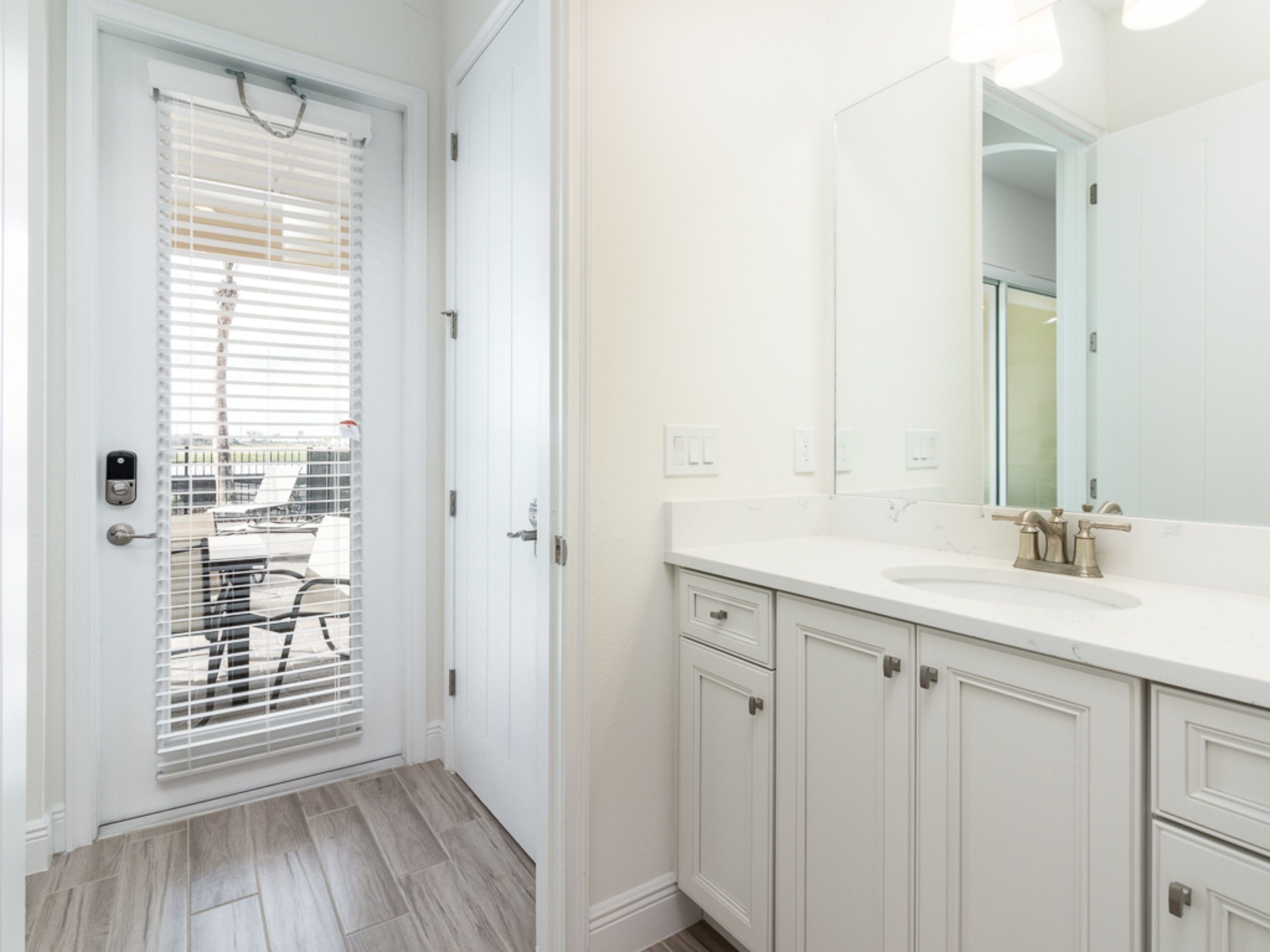 Un baño con muebles blancos, un espejo grande y piso de madera.