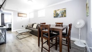 En moderne stue med spiseområde, sofa, fjernsyn og et billede på væggen.