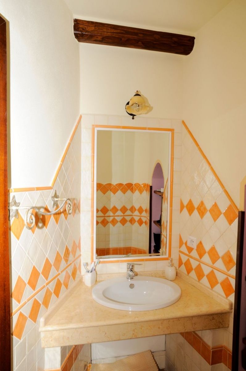 A bathroom with a white sink, orange and white patterned tiles, a mirror with a wooden frame, and a towel rack.