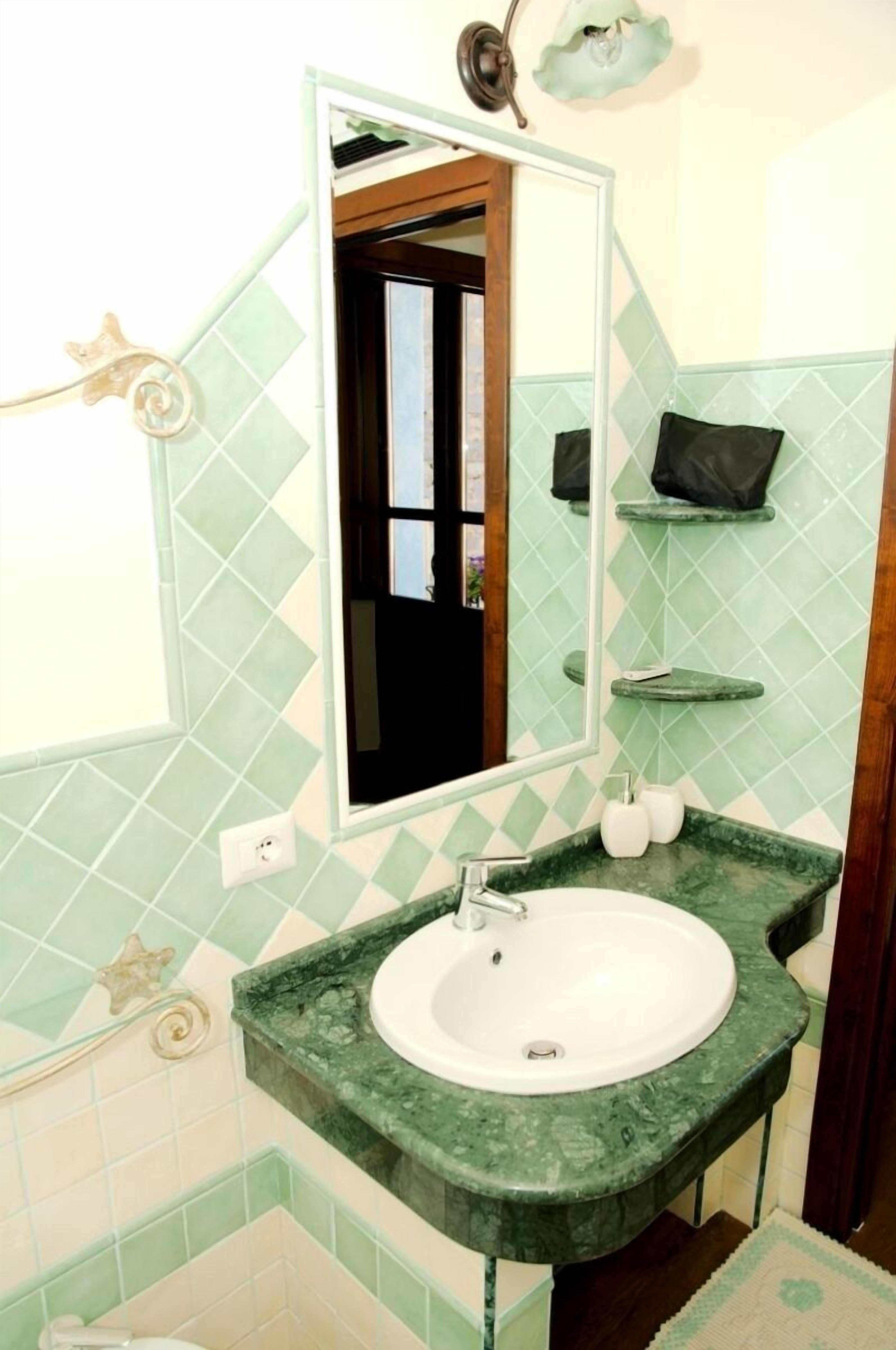 A bathroom with a green marble sink, a mirror, and a green-tiled wall.