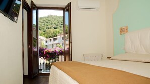 A bedroom with a bed, a window, and a view of a hillside with buildings. - L' affittacamere Funtanedda (Teti)