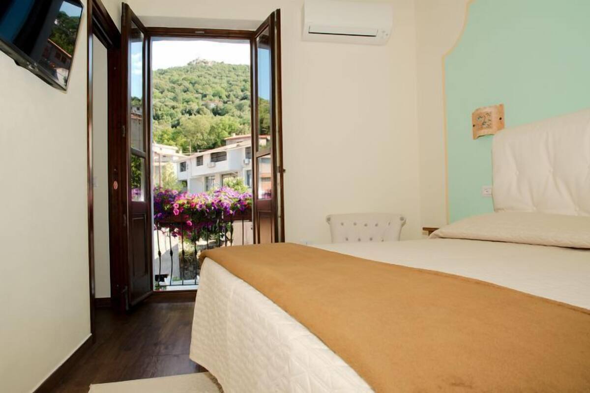 A bedroom with a bed, a window, and a view of a hillside with buildings.