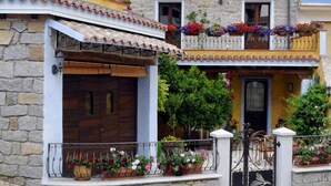 A two-story building with a stone facade, balconies with flower boxes, and a cobblestone ground. - L' affittacamere Funtanedda (Teti)