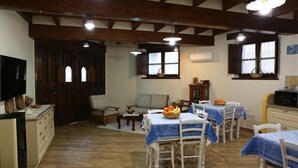 A dining area with wooden tables and chairs, a television, and a kitchen area with a refrigerator and cabinets. - L' affittacamere Funtanedda (Teti)