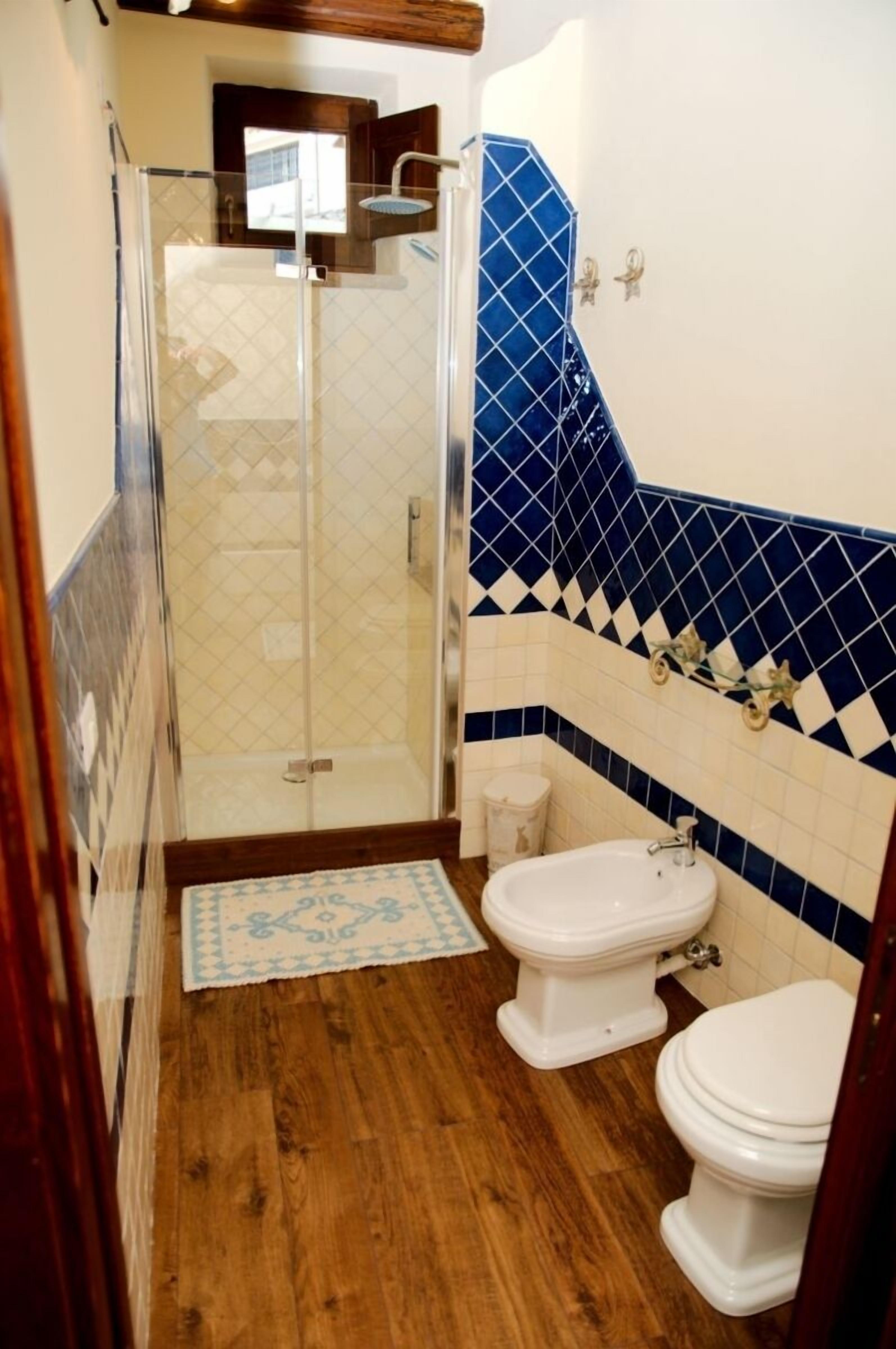 A bathroom with a glass-enclosed shower, two toilets, and a blue-tiled wall.
