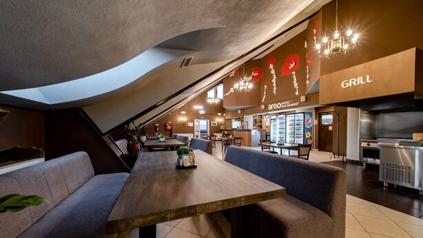 A restaurant with a long wooden table, cushioned seating, and a visible grill area. - Areo Hotel & Restaurant (Odorheiu Secuiesc)