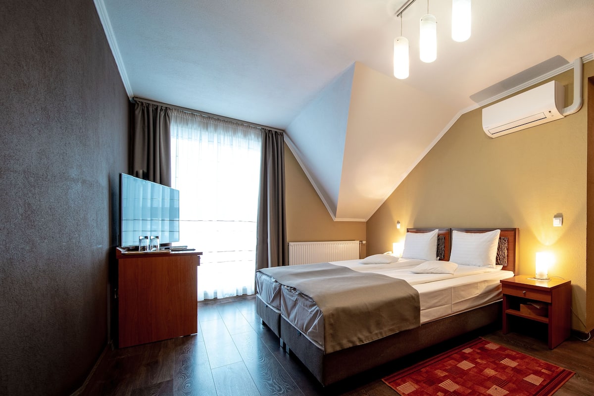 A bedroom with a bed, bedside tables, a TV, and a window with curtains.