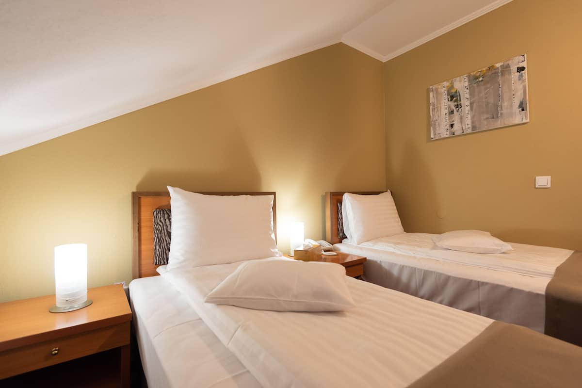 A hotel room with two beds, a nightstand with a lamp, and a wall-mounted artwork.