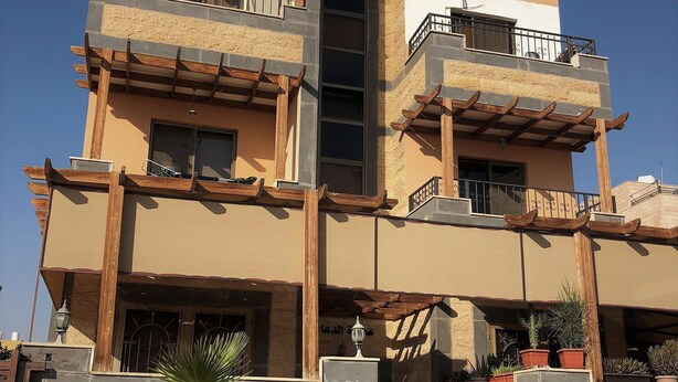 A multi-story building with balconies, a central vertical structure, and potted plants on the ground level. - Sea View Luxury Furnished Flat (Aqaba)