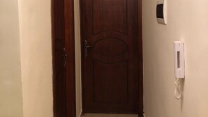 A narrow hallway with a wooden door at the end, a wall-mounted intercom, and a light switch. - Sea View Luxury Furnished Flat (Aqaba)