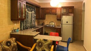 A compact kitchen with wooden cabinets, a built-in stove, and a refrigerator. - Sea View Luxury Furnished Flat (Aqaba)